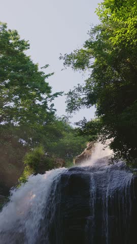Beautiful waterfall with sun rays in a lush green forest in Oita. A mystical video of Ameushi Falls in Taketa, Oita, Japan, with dramatic sunbeams (crepuscular rays) piercing through the trees. The powerful waterfall, surrounded by moss-covered rocks and fresh greenery, creates a serene and therapeutic atmosphere. Perfect for nature, travel, wellness, and healing concepts. with natural sound