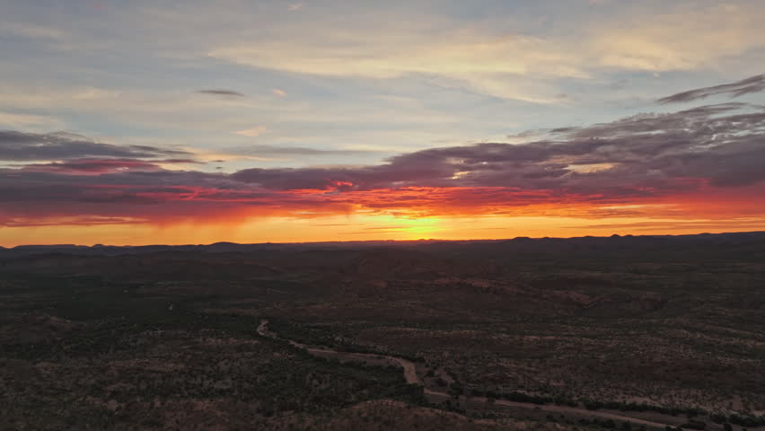 Drone footage of a deep red sunset glowing over a dark Namibian desert plain, a dry riverbed tracing the highland floor below.