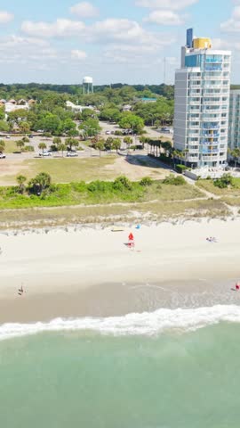 Vertical screen. Beachgoers enjoy sunny day at Myrtle Beach, South Carolina, with colorful umbrellas and ocean waves in the background
