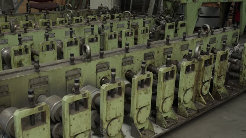 Long row of green roll forming stands with rollers on an industrial tube mill in a metal factory