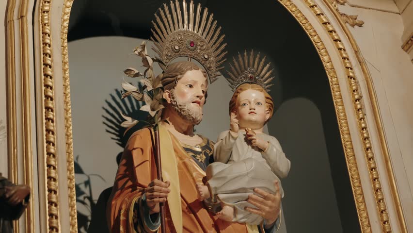 Carved statue of crowned Saint Joseph holding the Christ child with silver halos in a church
