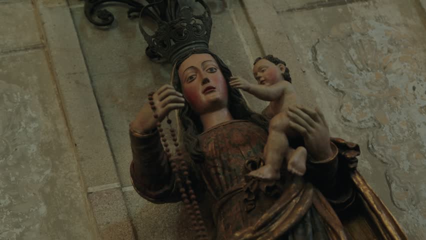 Carved statue of crowned Virgin Mary holding the Christ child and a rosary inside a church