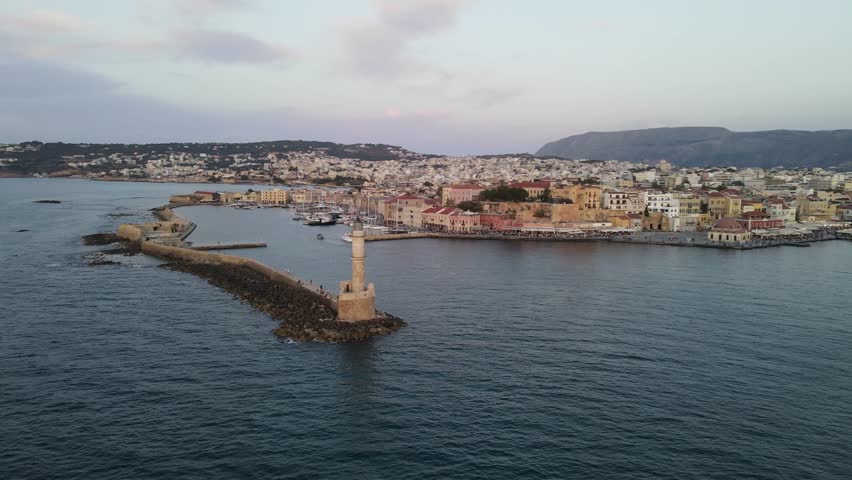 Chania, Crete. Aerial drone view of the historic Venetian harbor and lighthouse. Panoramic cityscape showing the old town and the Mediterranean coastline at dusk.