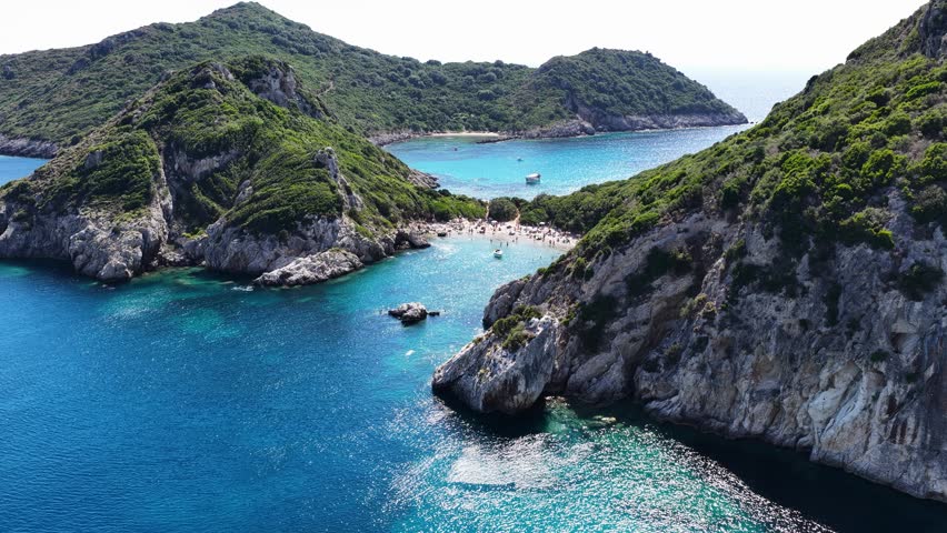 Drone view of Porto Timoni double beach in Corfu Greece. Scenic twin bays with crystal clear turquoise water, green lush hills, rocky coast and tourists sunbathing on summer holiday
