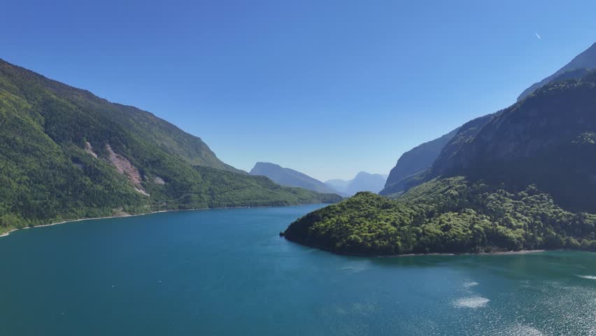 Skimming closer to the water line, this drone flight offers an intimate, low-angle glide over the deep blue surface of Lago di Molveno. The camera movement captures the gentle texture of the lake while looking forward into the majestic V-shaped valley formed by the surrounding Alps. The composition provides an organic sense of movement, drawing the viewer deep into the scenic landscape of Northern Italy. This unique perspective is perfect for high-impact travel vlogs, action-adventure intros, vacation ads, and transition scenes in nature documentaries.

