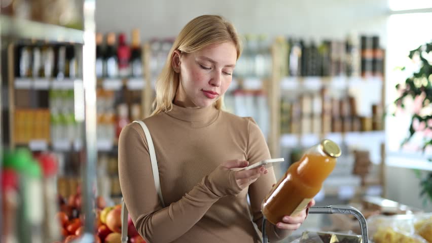 Girl scan QR code, take reading peach juice label using phone camera in shop. Client inspect juice plastic bottle product, view manufacturer information using mobile application