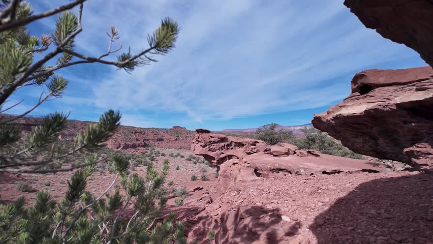 Drone video captures dramatic red desert sandstone formations, rough rocky terrain, and sparse green vegetation near Moab, Utah on a crystal clear, sunny day with vibrant blue skies.