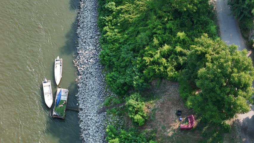 Small boats moored along the Po River beside a riprap embankment at the Maginot riverside area near Castelvetro Piacentino, Piacenza, Emilia-Romagna, Italy, with woodland and outdoor seating, static