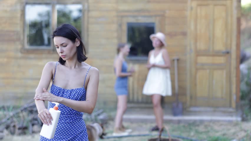 Young woman in dress applying sunscreen outside country house