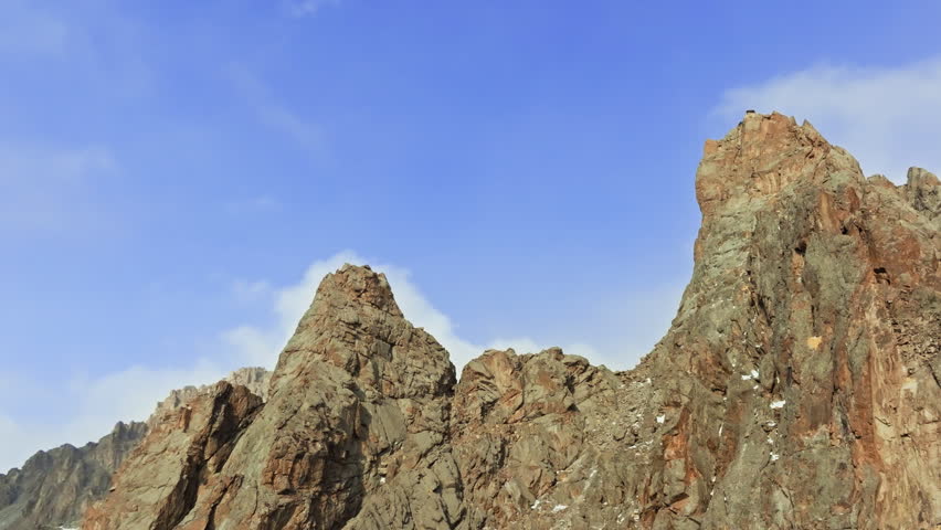 Rocky mountain peaks tower majestically against clear blue sky. Small structure on summit adds a sense of remote serenity and awe-inspiring beauty.