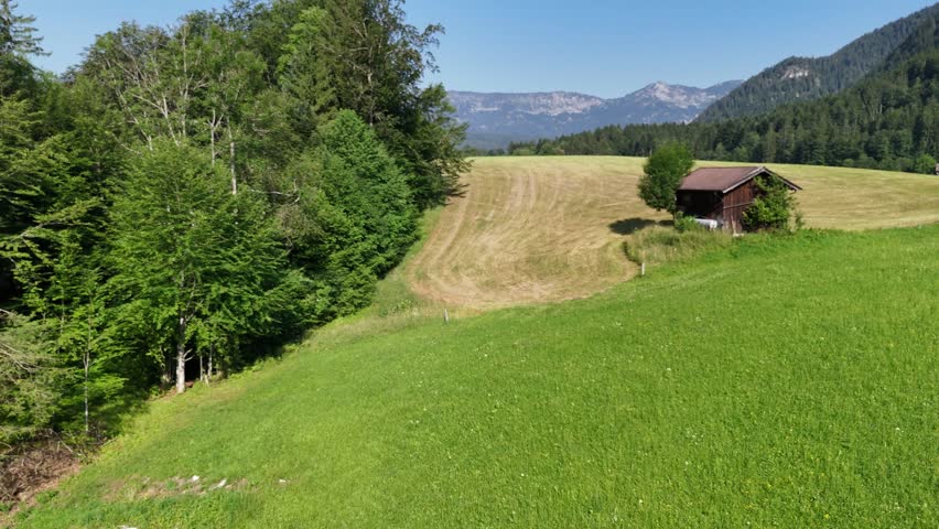 Picturesque landscape with a wooden house in the middle of a field against the background of mountains and forest. View of the countryside in the foothills. Mowed field, green forest and mountains