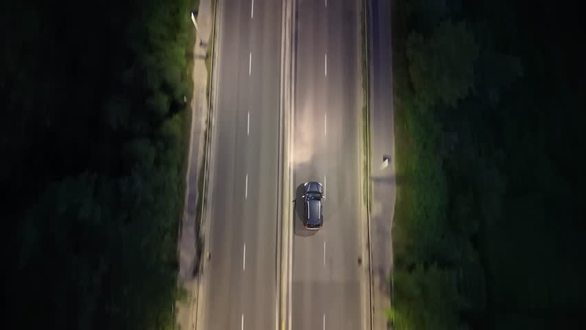 Aerial view of a black car driving on a well-lit road at night, showcasing the smooth flow of traffic with a truck approaching from the opposite direction