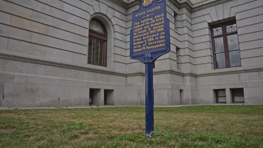 Tilt up from Pennsylvania State Capitol signage and grand staircase toward the historic capitol building in Harrisburg showcasing government architecture and civic landmark details.