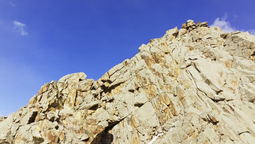 Majestic mountain rock face rises against a clear blue sky. Drone view with arc movement.