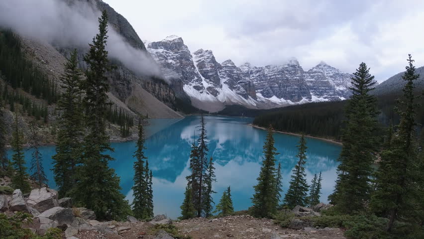 Clouds drift around the Valley of the Ten Peaks in a time lapse over Moraine Lake’s turquoise water and dark conifer slopes.