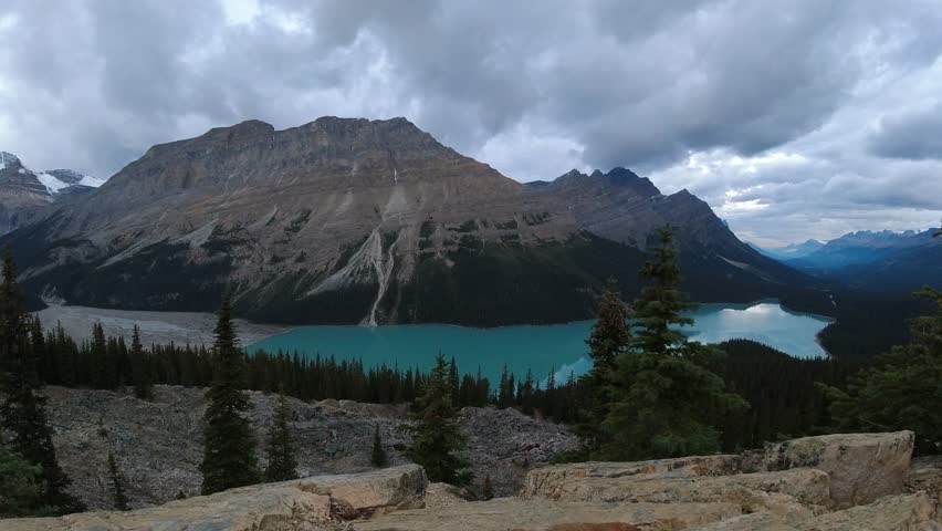 Clouds brighten as sunrise light slowly sweeps across mountains above turquoise Peyto Lake in this wide timelapse shot.
