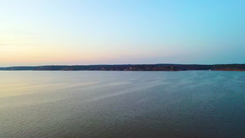 Aerial view over Lake Hartwell, Georgia and South Carolina, showing calm reservoir water, wooded shoreline, distant homes, and pastel dusk sky over the lake.