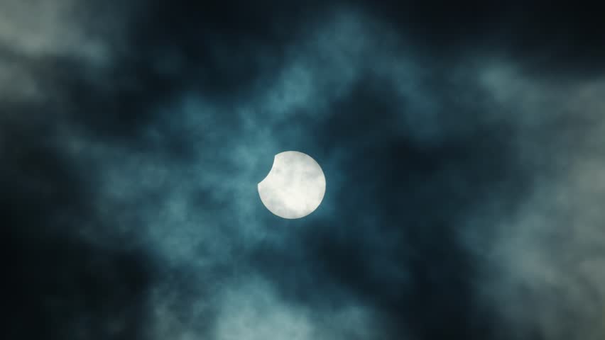Partial solar eclipse visible through dark stormy clouds in sky.