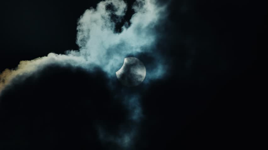 Partial solar eclipse visible through dark stormy clouds in sky.