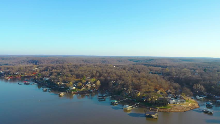 Scenic Dale Hollow Lake drone view with lakefront houses, covered boat slips, still reservoir water, tree-lined banks, and a quiet residential shoreline at sunset.
