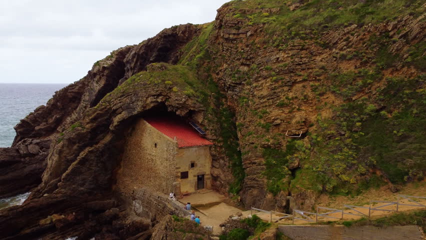 Aerial drone view of Santa Justa Hermitage, a unique chapel built inside a coastal cliff cave in Ubiarco, near Santillana del Mar, Cantabria, Northern Spain. High quality 4k footage