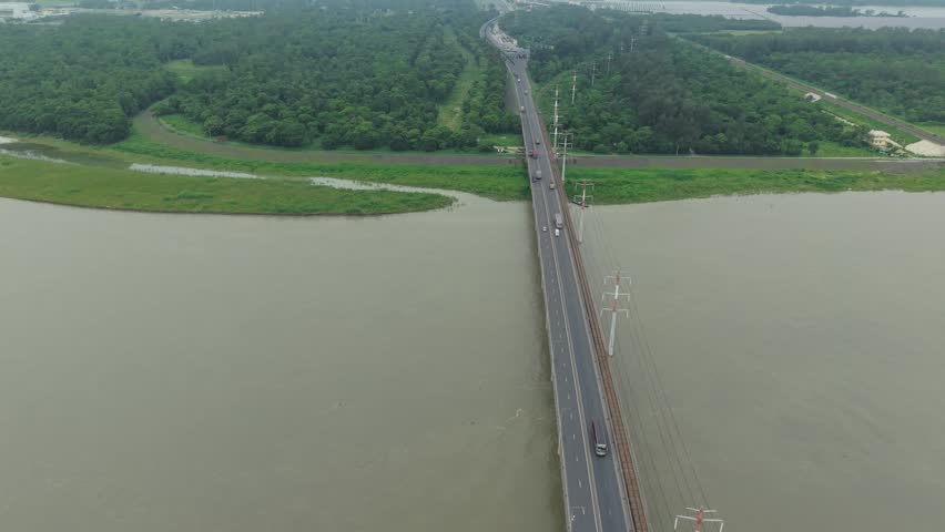 Aerial view of a long bridge crossing over a wide river surrounded by lush green tropical forest