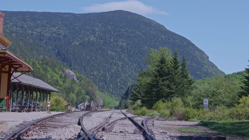 Historic mountain railway Crawford Notch Station with train tracks leading toward forested White Mountain National Forest mountainous environment, New Hampshire, US