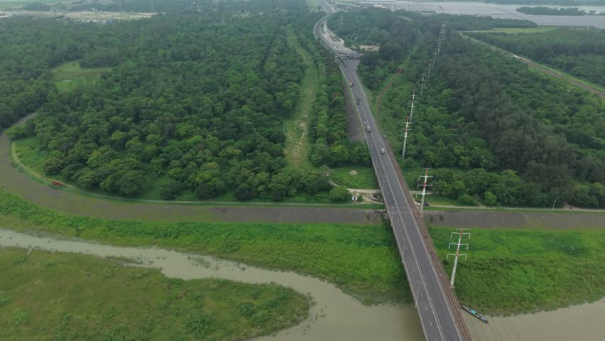 Aerial view of a long road bridge crossing over a river through a lush green forest landscape