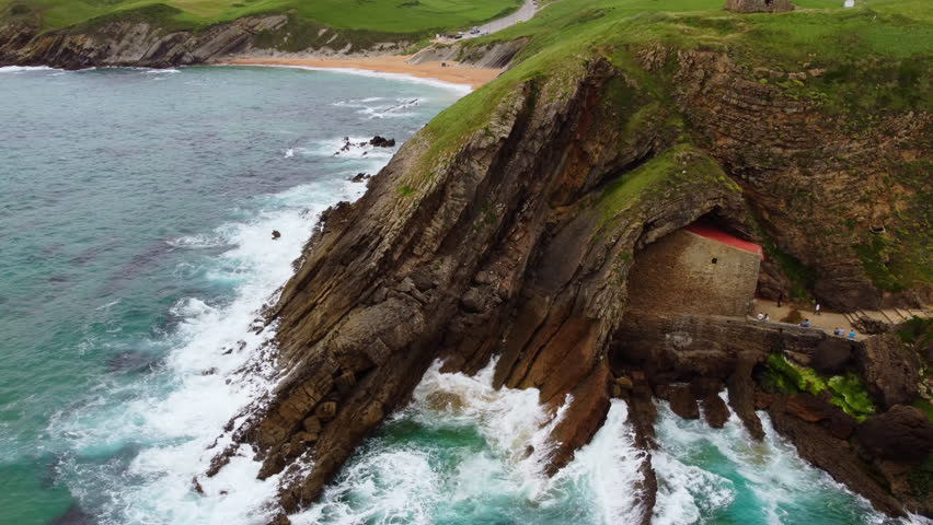 Aerial drone view of Santa Justa Hermitage, a unique chapel built inside a coastal cliff cave in Ubiarco, near Santillana del Mar, Cantabria, Northern Spain. High quality 4k footage