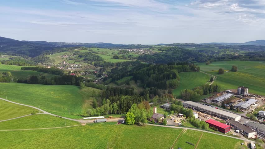 Aerial view green hills village valley, springtime panorama over rolling farmland and dense forest, winding