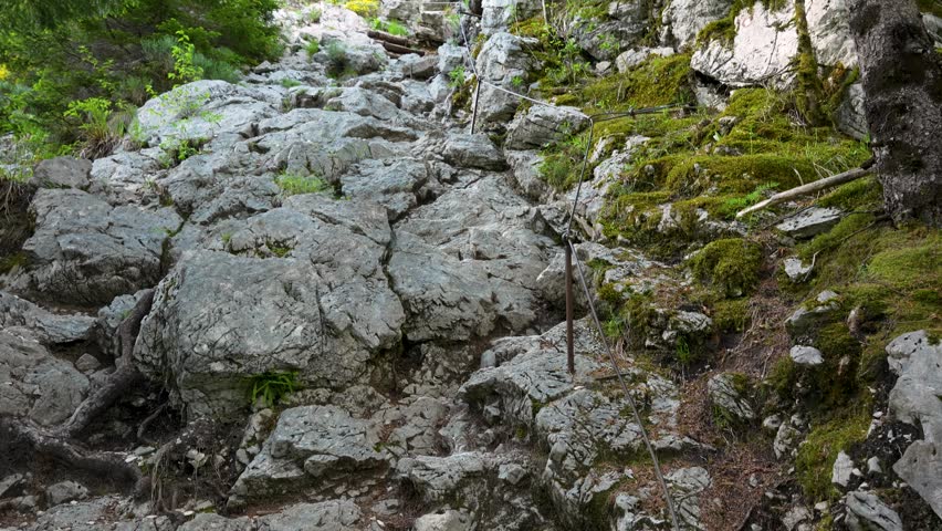 Rocky mountain trail leading through forest toward the source of the Soca River, metal spikes line trail with guide rope