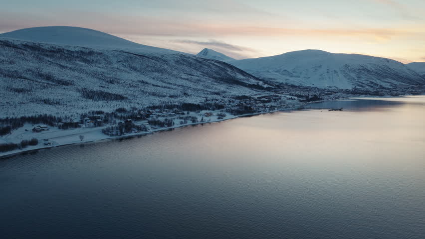 Snowy Arctic mountains rising above a glassy fjord at sunset, drone
