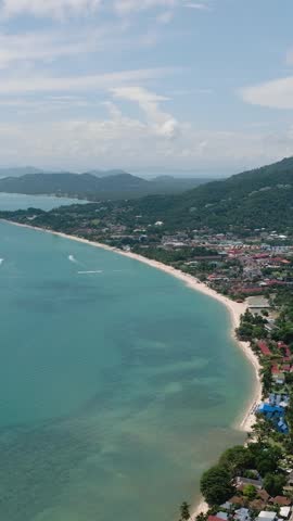 A sandy beach lined with tropical greenery and turquoise waters under a bright sky. Ko Samui, Thailand.