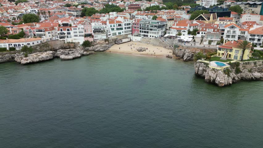 Aerial drone panorama of Cascais, Portugal, showing the Atlantic coastline, red rooftops, seaside buildings and beaches under soft grey weather. Scenic Portuguese Riviera travel footage