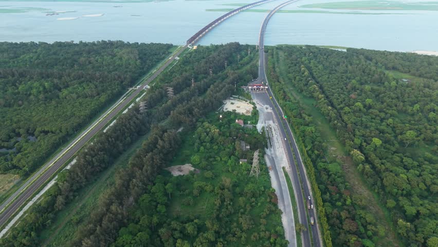 Aerial view of a long bridge crossing over the sea surrounded by green forest trees