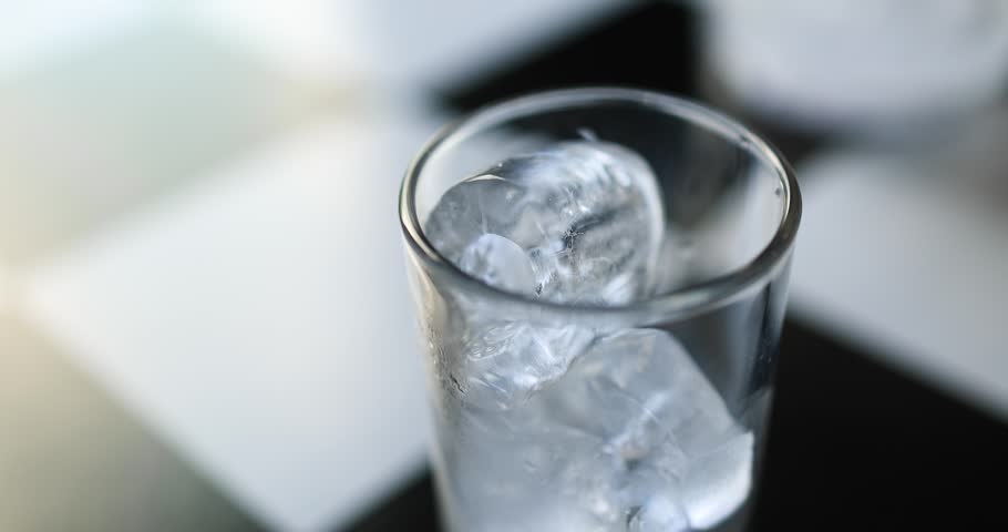 Clear water pouring from a glass bottle into an ice-filled glass. Close-up shot, freshness, purity, hydration, healthy lifestyle, and refreshing beverage