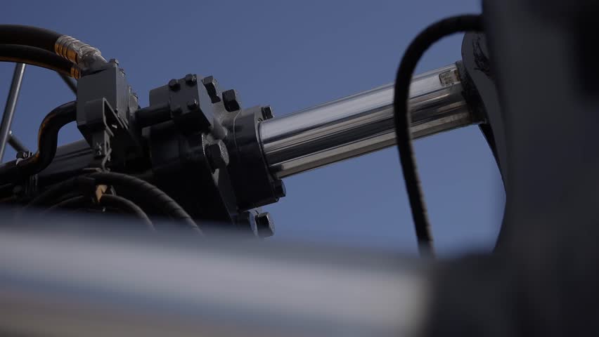 Hydraulic cylinder piston extending on industrial machinery arm against clear blue sky.