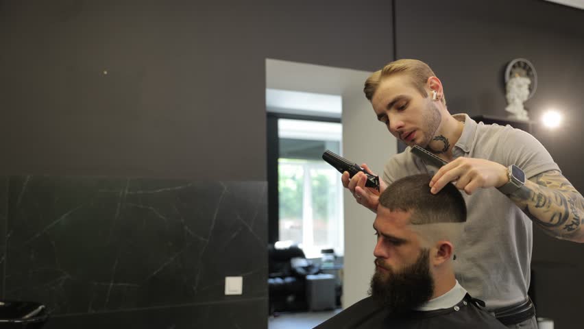 Tattooed barber giving haircut with clipper