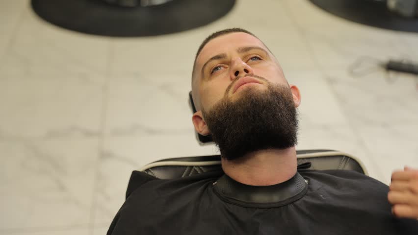 Tattooed barber giving haircut to bearded man in barbershop