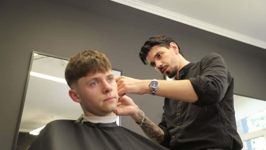 Tattooed barber giving haircut to young male client