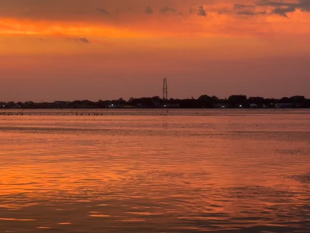 A fishing boat docked at a pier at sunset with a vibrant orange sky reflected in the calm ocean water.