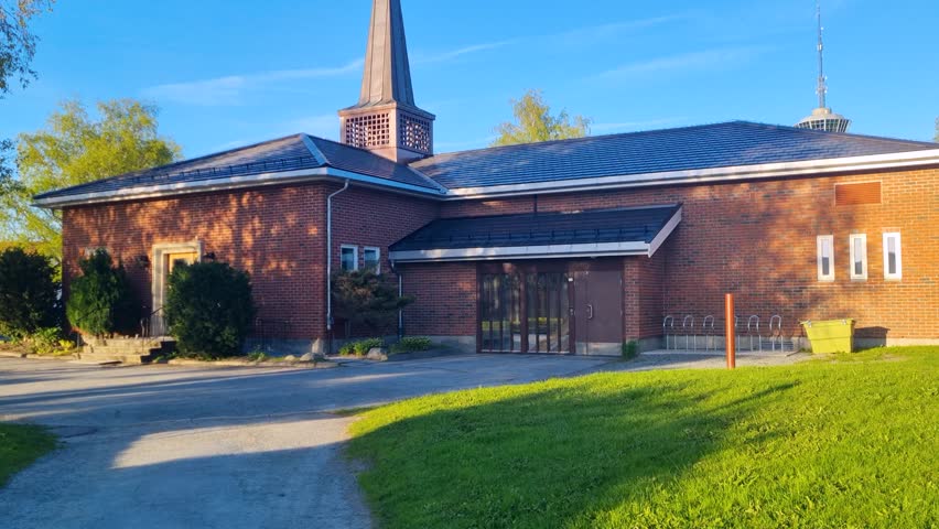 Berg Arbeidskirke in Trondheim, Norway, under a bright sunny sky, with its distinctive church tower standing out against the blue backdrop. A notable example of modern Scandinavian church architecture