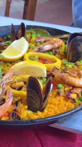 Paella Valenciana served in a traditional wide pan, with shrimp, mussels, peas. Traditional Spanish seafood paella with prawns mussels and lemon slices in a large frying pan