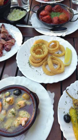 Traditional Spanish tapas variety on a wooden table including calamari and meatballs
