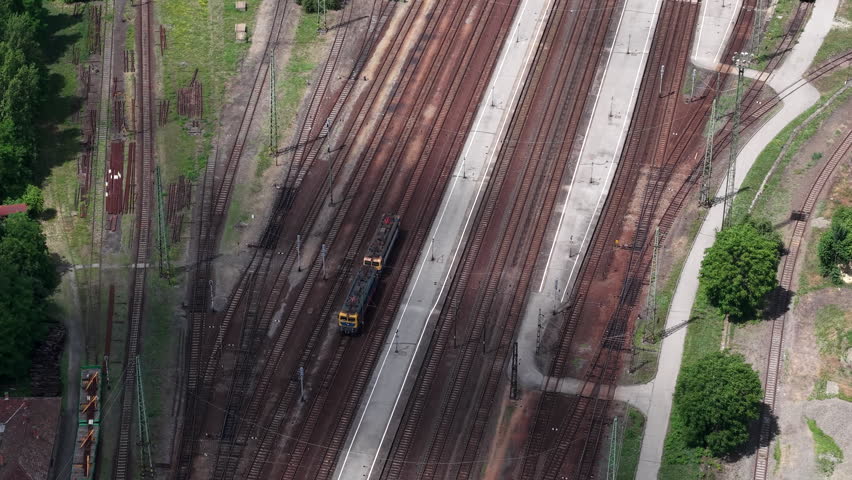 Aerial view of a railway station in Hungary showing multiple parallel tracks and a locomotive moving through the platform area.