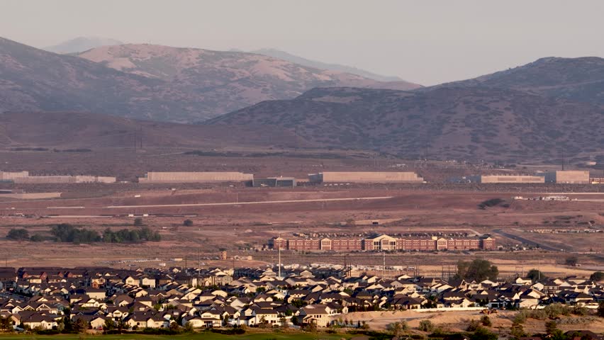 High altitude aerial view of Lehi suburbs, Camp Willimas, and the Utah Data Center against the Oquirrh mountains on a hazy day
