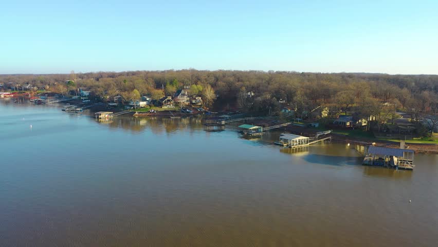 High aerial above Lake of the Ozarks, Missouri, capturing a lakeside neighborhood, shoreline homes, narrow coves, private piers, and tranquil water in soft sunset color.