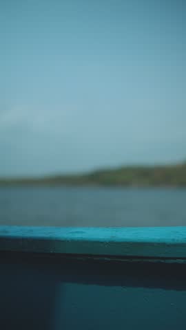 Blue boat moves across calm water with distant green shoreline under clear sky