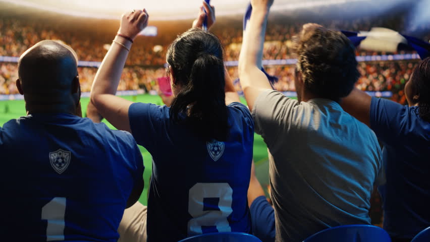 Soccer supporters cheer in packed stadium stands during a football match, creating loud crowd energy and team support.