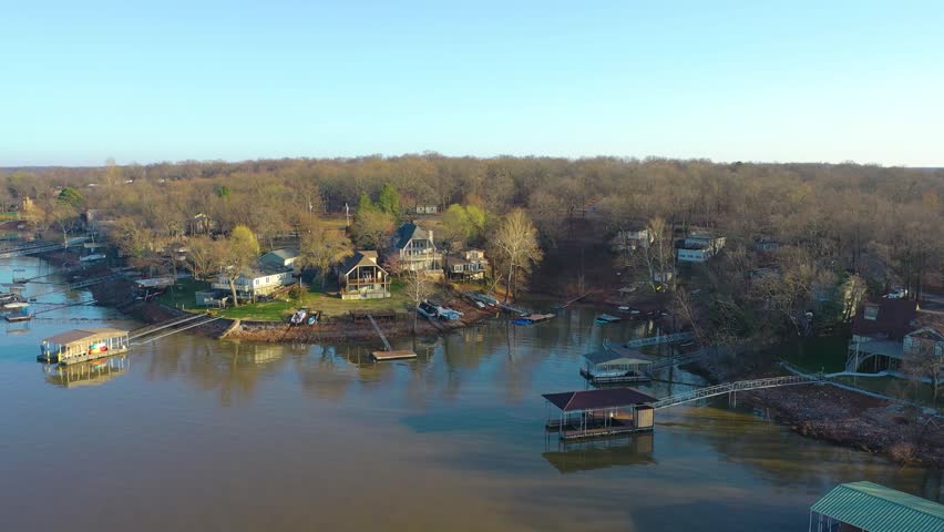 Aerial view of Norris Lake in Tennessee with waterfront houses, covered boat docks, still blue water, tree-lined shoreline, and a calm residential bay at golden hour.